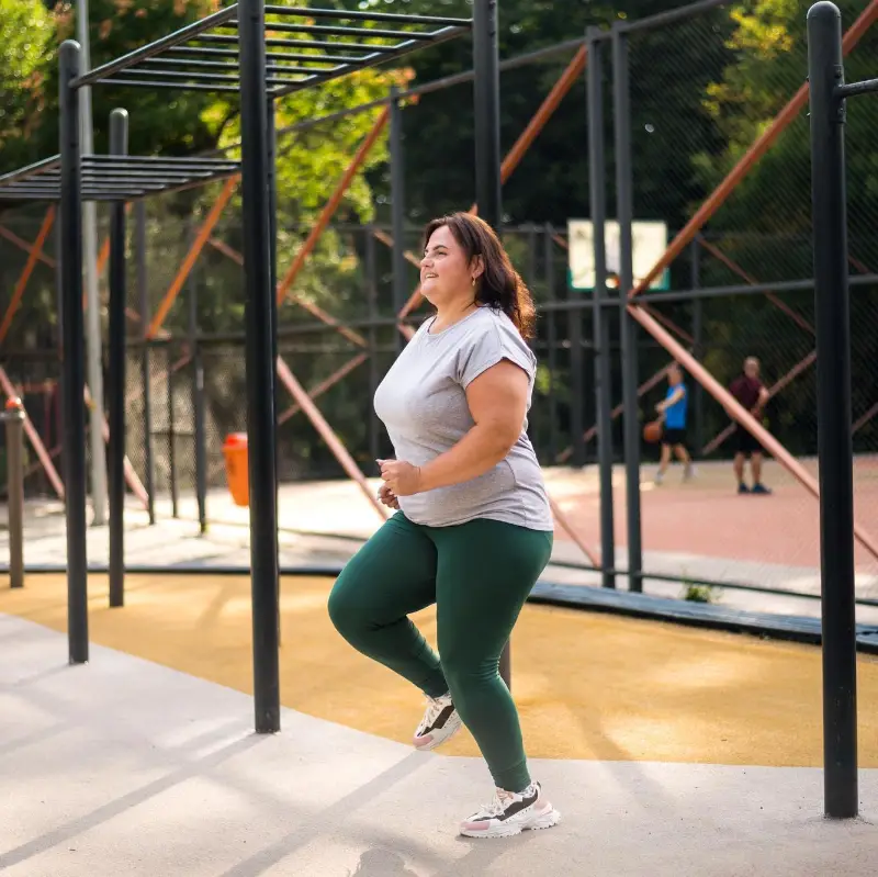 Smiling woman with overweight in a tracksuit doing exercises on a sports field in a park
